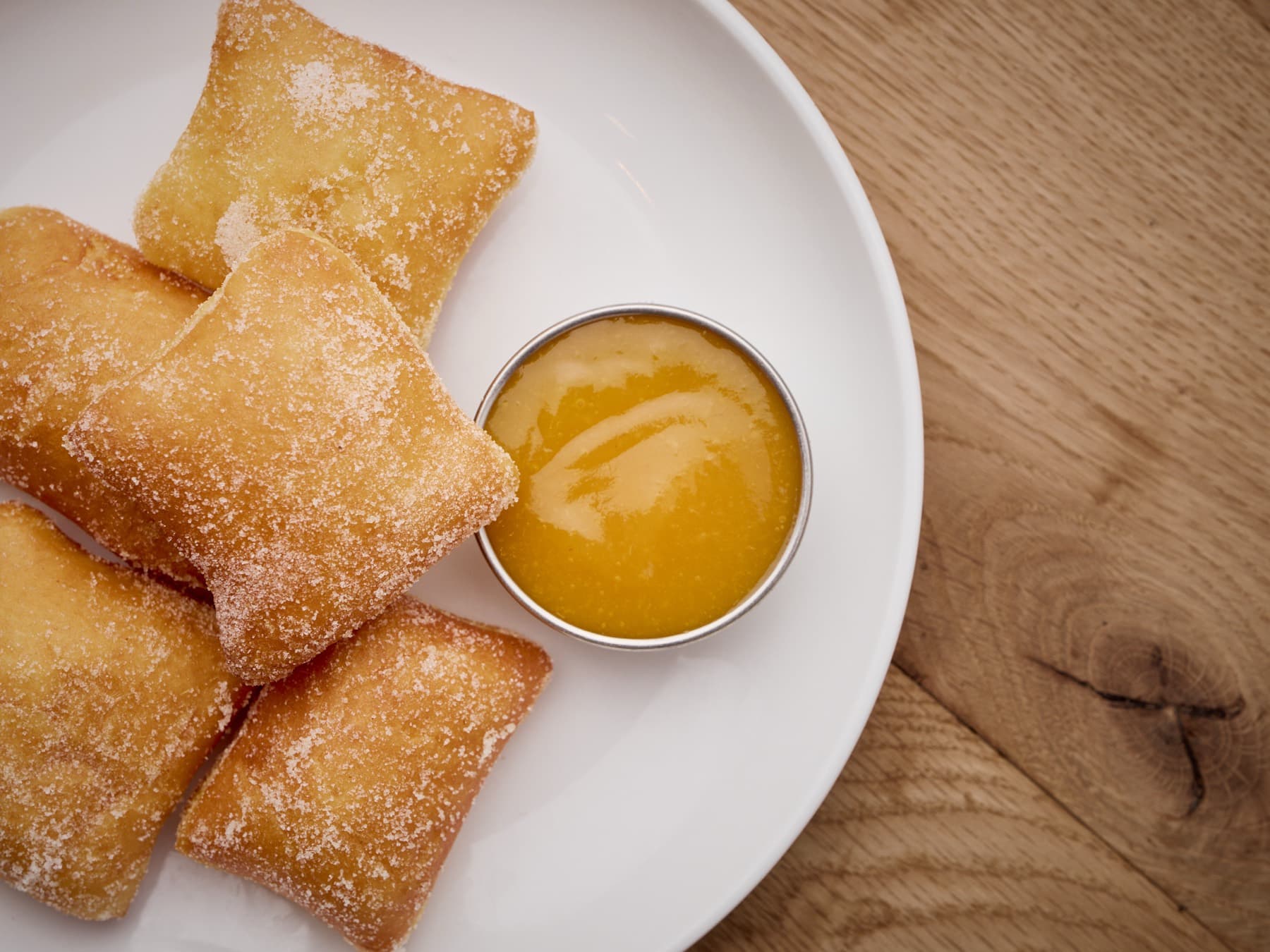 A sugared beignet being dunked into citrus curd