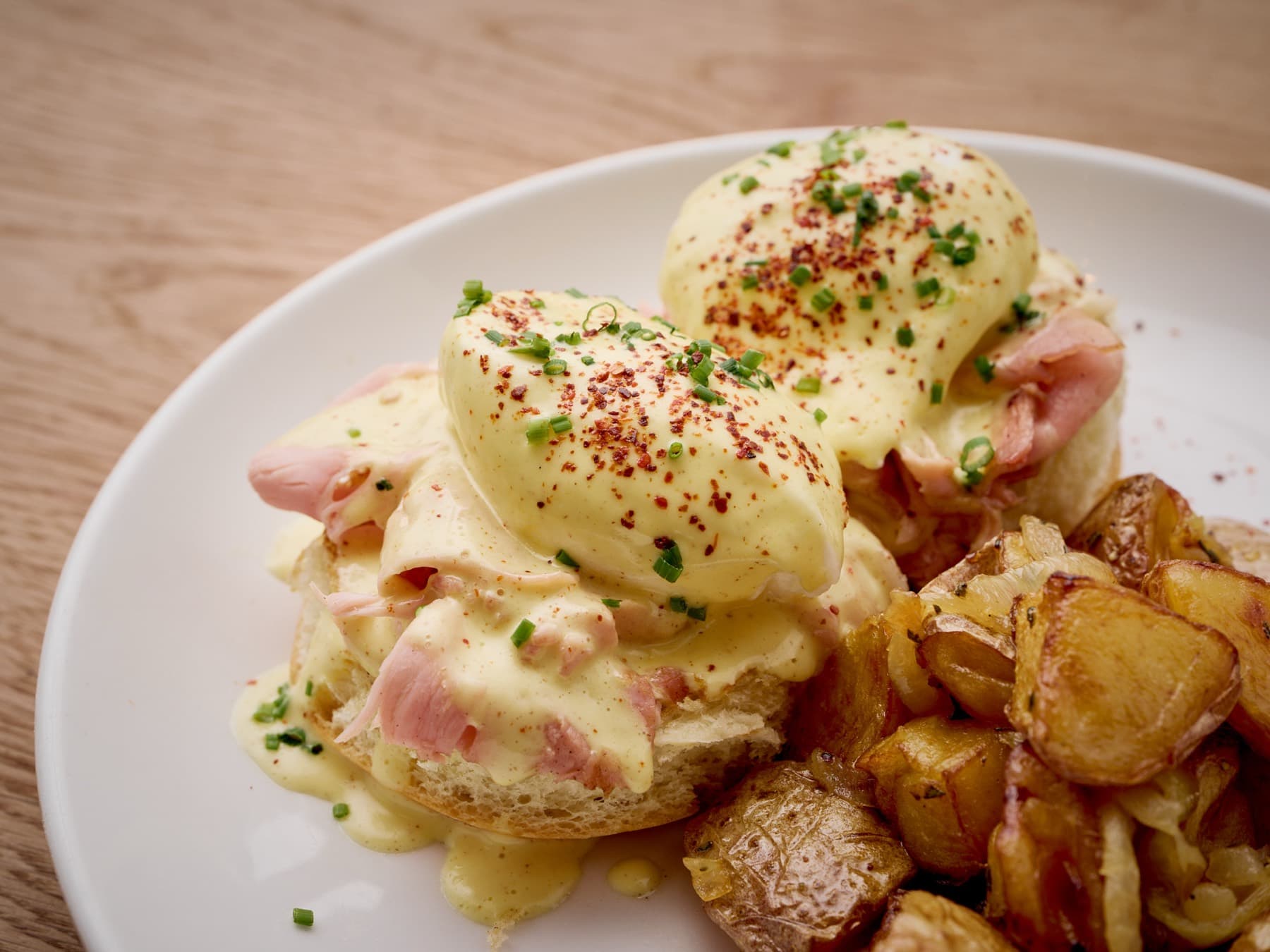 Eggs Benedict draped in hollandaise with chives and crispy potatoes