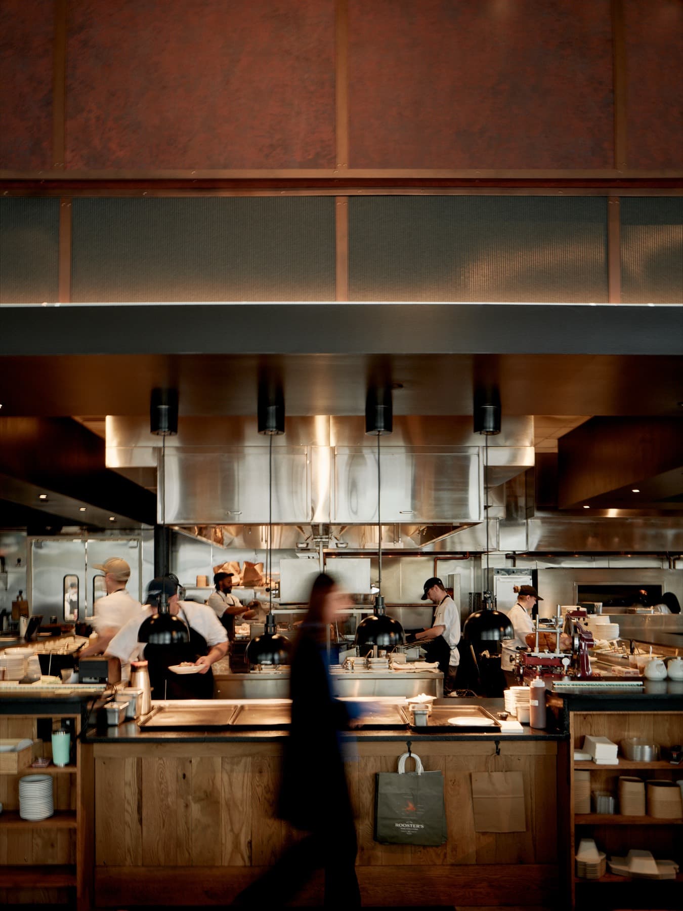 The Ballantyne open kitchen framed under its oxblood canopy, a server in motion