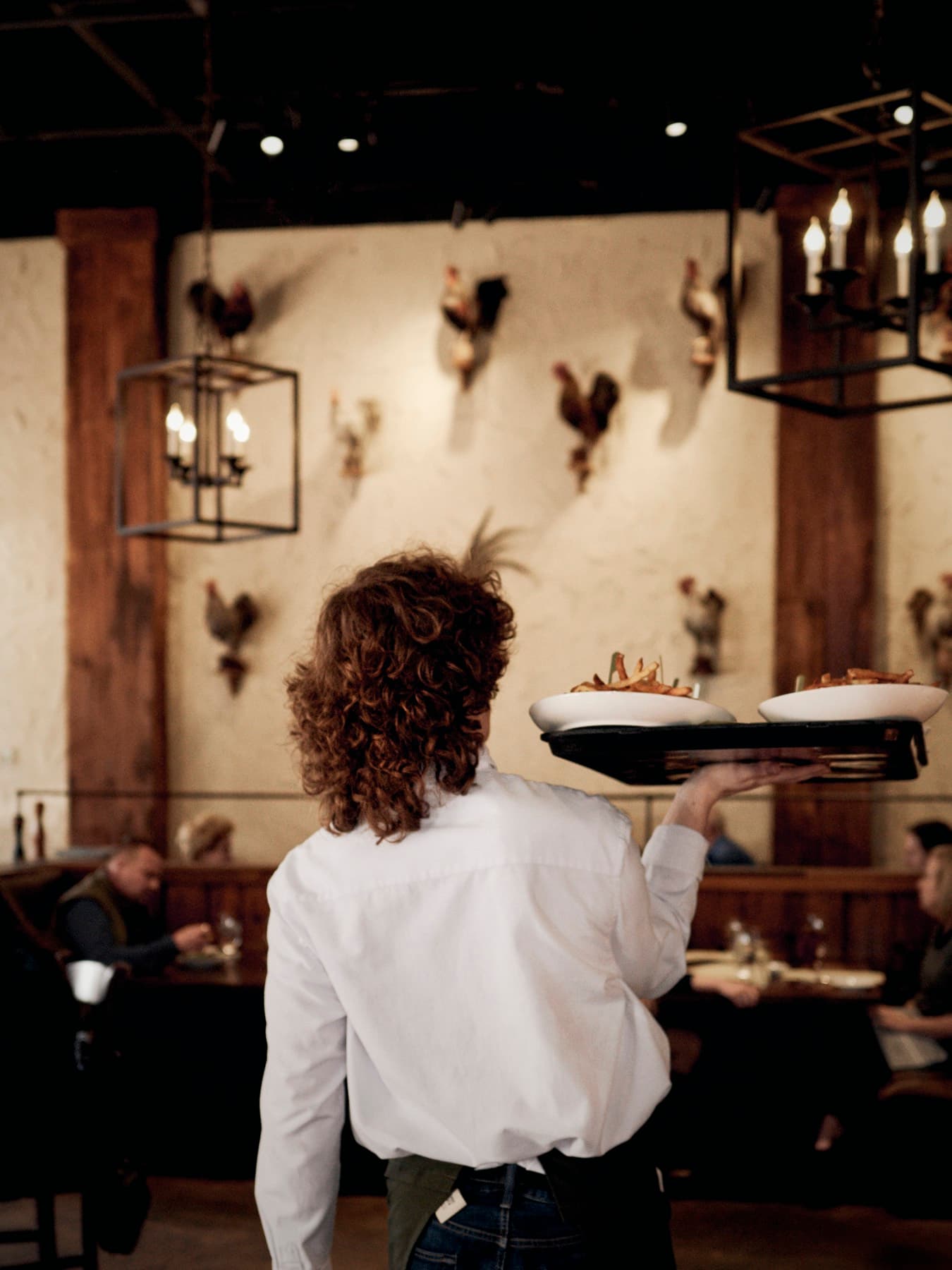 A server carrying two plates through the lantern-lit dining room