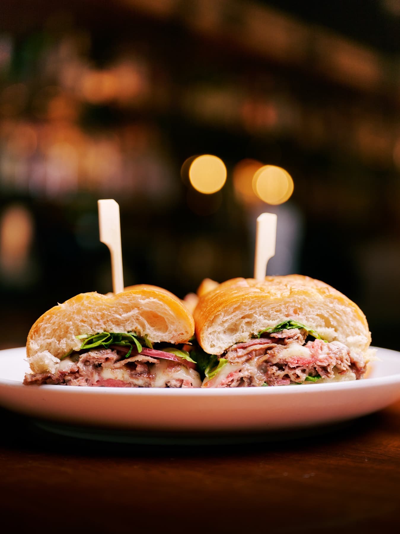 Shaved roast beef croissant sandwich halves on picks at the bar