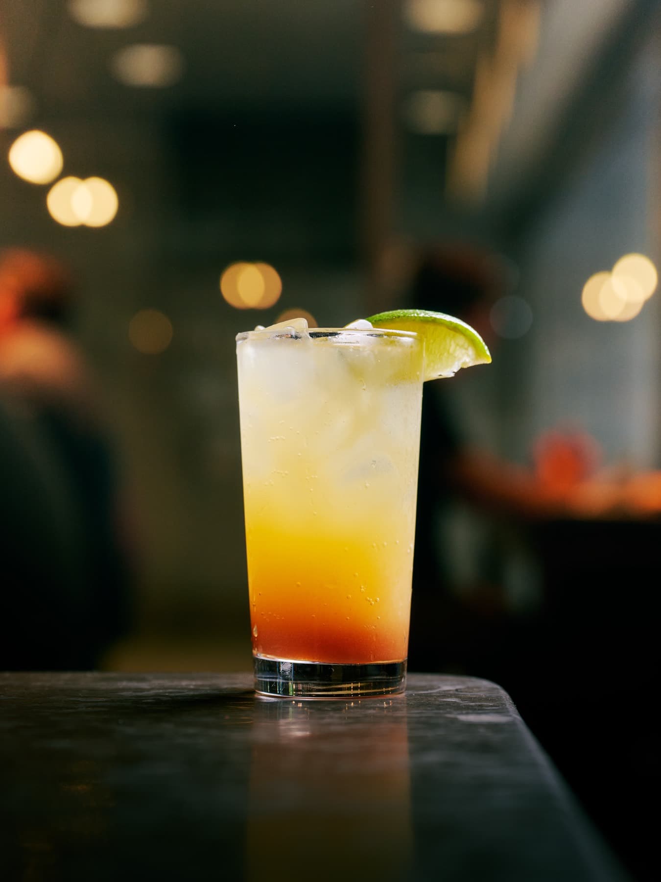 A sunset-layered highball cocktail with lime on the marble bar edge